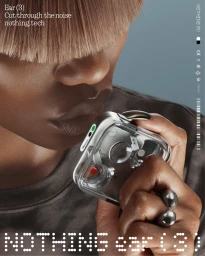 Close-up of a person holding a transparent wireless earbud charging case, wearing a dark grey t-shirt against a grey background