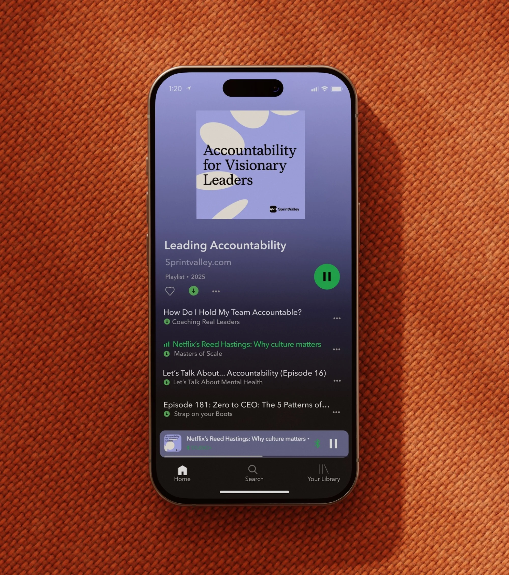 Smartphone displaying the Spotify app, featuring a podcast titled 'Accountability for Visionary Leaders' on an orange fabric background.