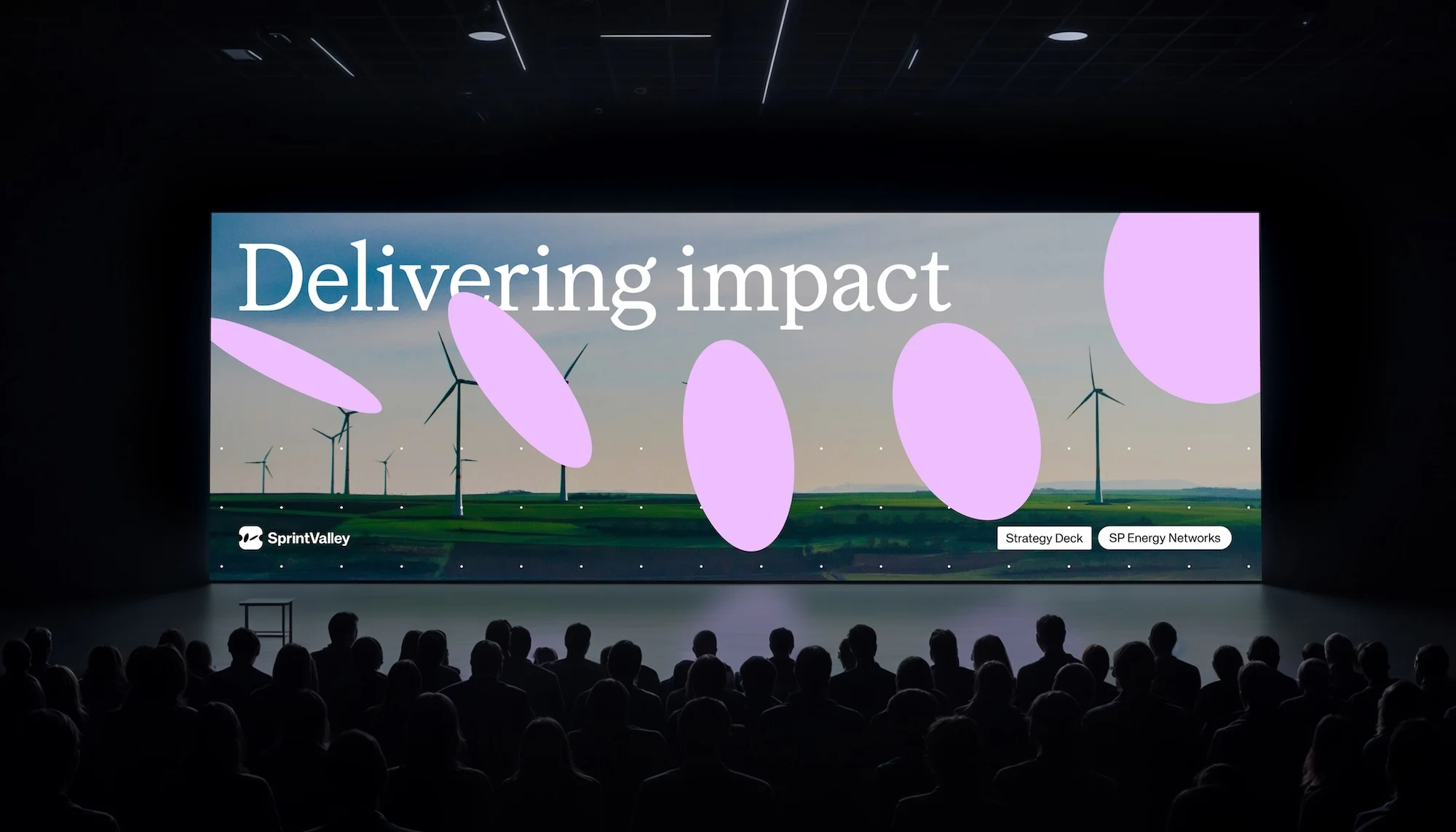 Audience views screen displaying wind turbines and Sprint Valley logo; event setting in auditorium with stage and presentation.