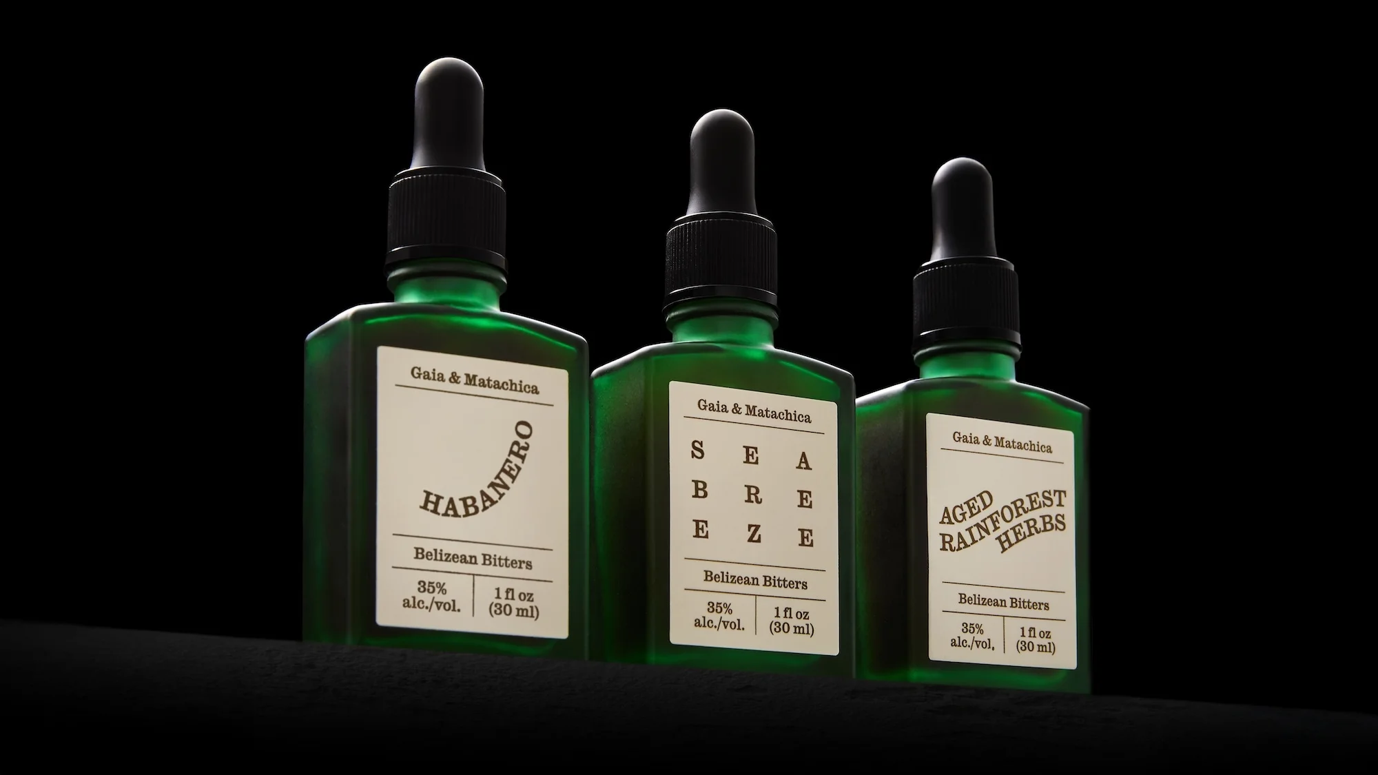 Three green glass bottles with black dropper caps sit on a black surface, each labeled with the text 'Gaia & Matachica' and a unique name.