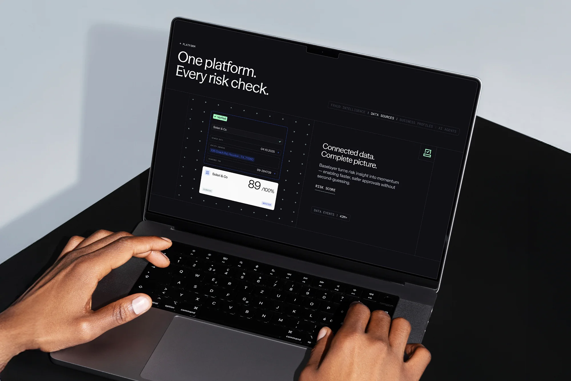Close-up of a person using a laptop with a sleek, dark interface displaying data and financial insights. The screen reads 'One platform. Every risk check.'