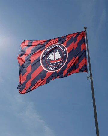 S.C. Gjoa Soccer flag featuring a sailboat logo against a clear blue sky on a sunny day with a modern graphic pattern.
