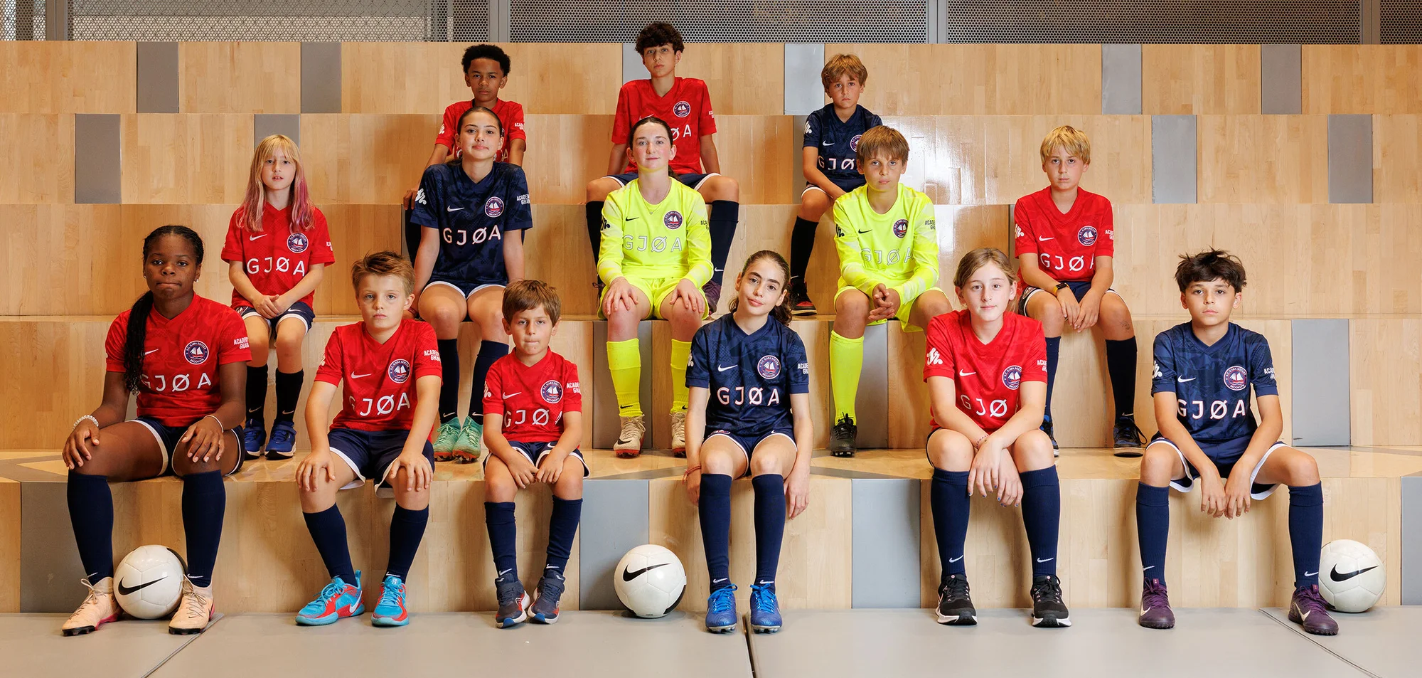 Group of young soccer players in team uniforms sitting on steps. The athletes are wearing matching jerseys and shorts with athletic shoes.