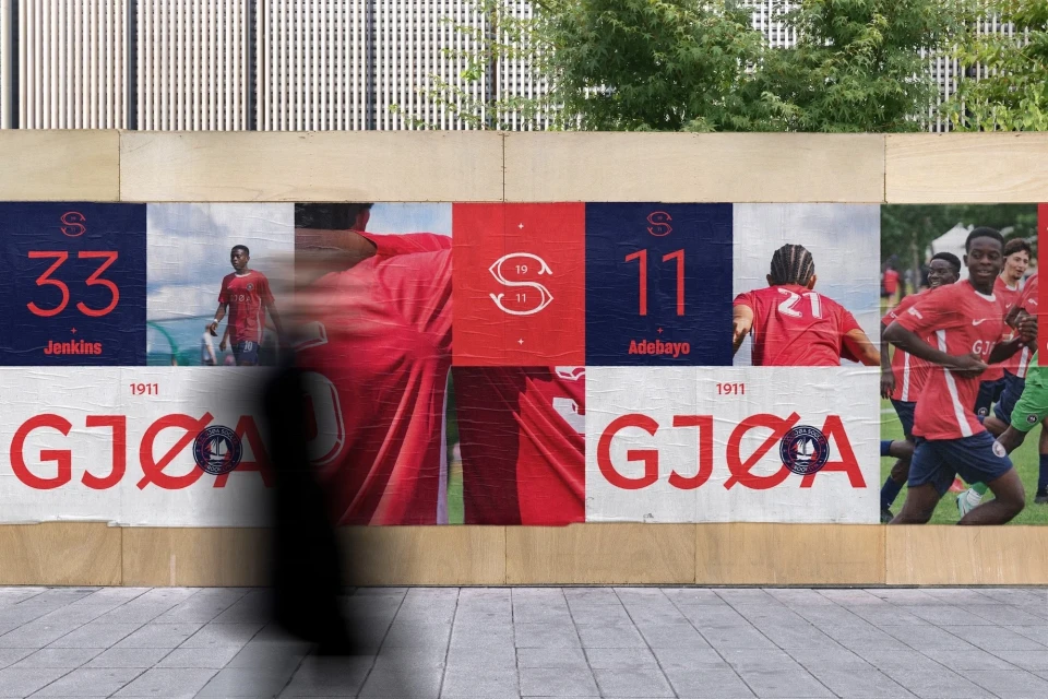 Eye-level shot of a sidewalk-affixed advertisement featuring soccer players in action, promoting a team with red and blue colors.