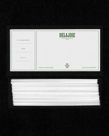 Stack of printed cards with green lettering featuring the words 'DELAJOIE STUDIO DE CREATION PARIS' against a black background.