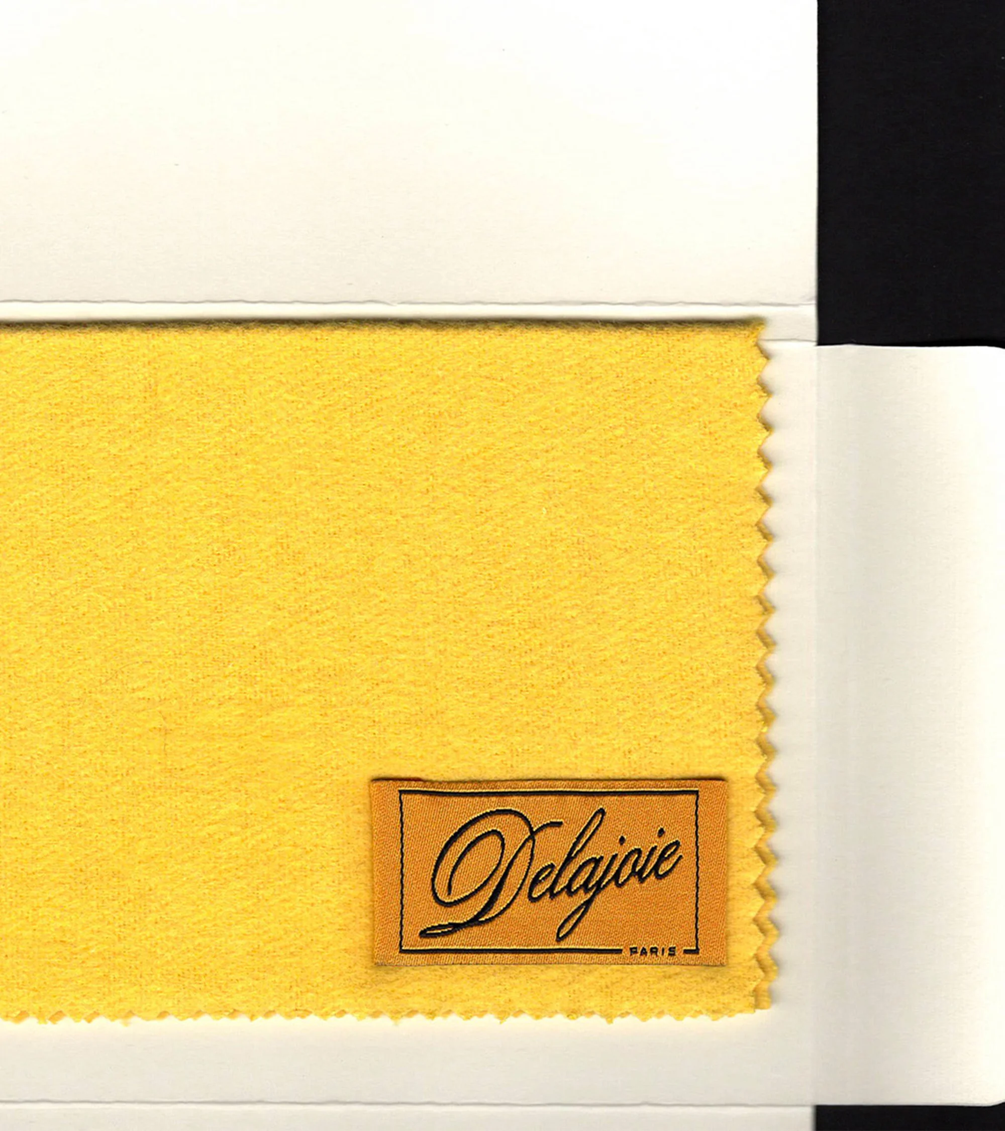 Close-up of a yellow fabric swatch with 'Delajoie Paris' label, presented on a white card, emphasizing textile details and color accuracy.