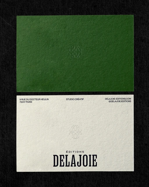 Two business cards, one green and one white, displayed on a black surface, with the text 'DELAJOIE' prominently featured on the white card.