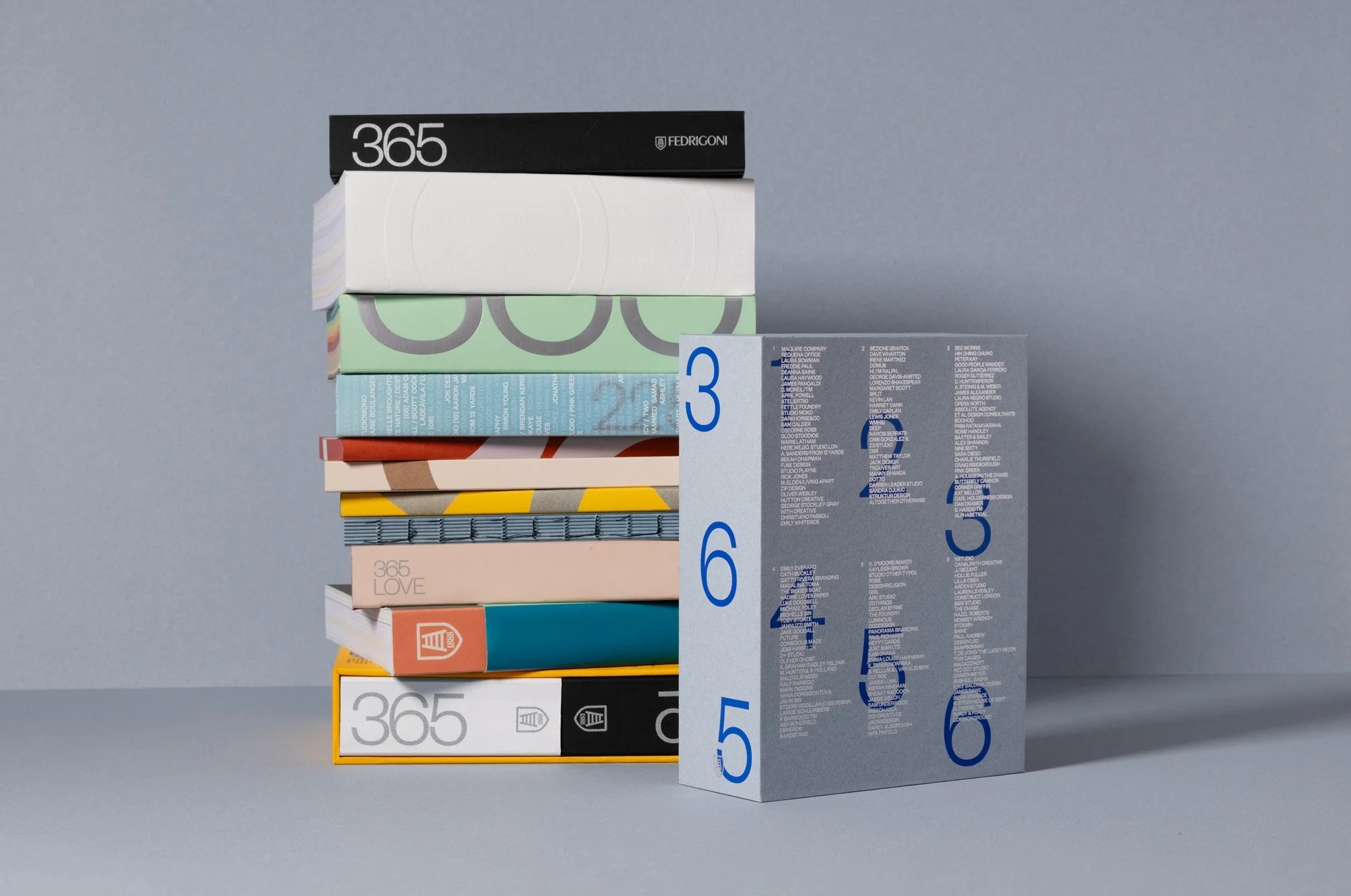 Stack of colorful paper sample books with geometric patterns, next to a gray book with numbers, on a gray surface.