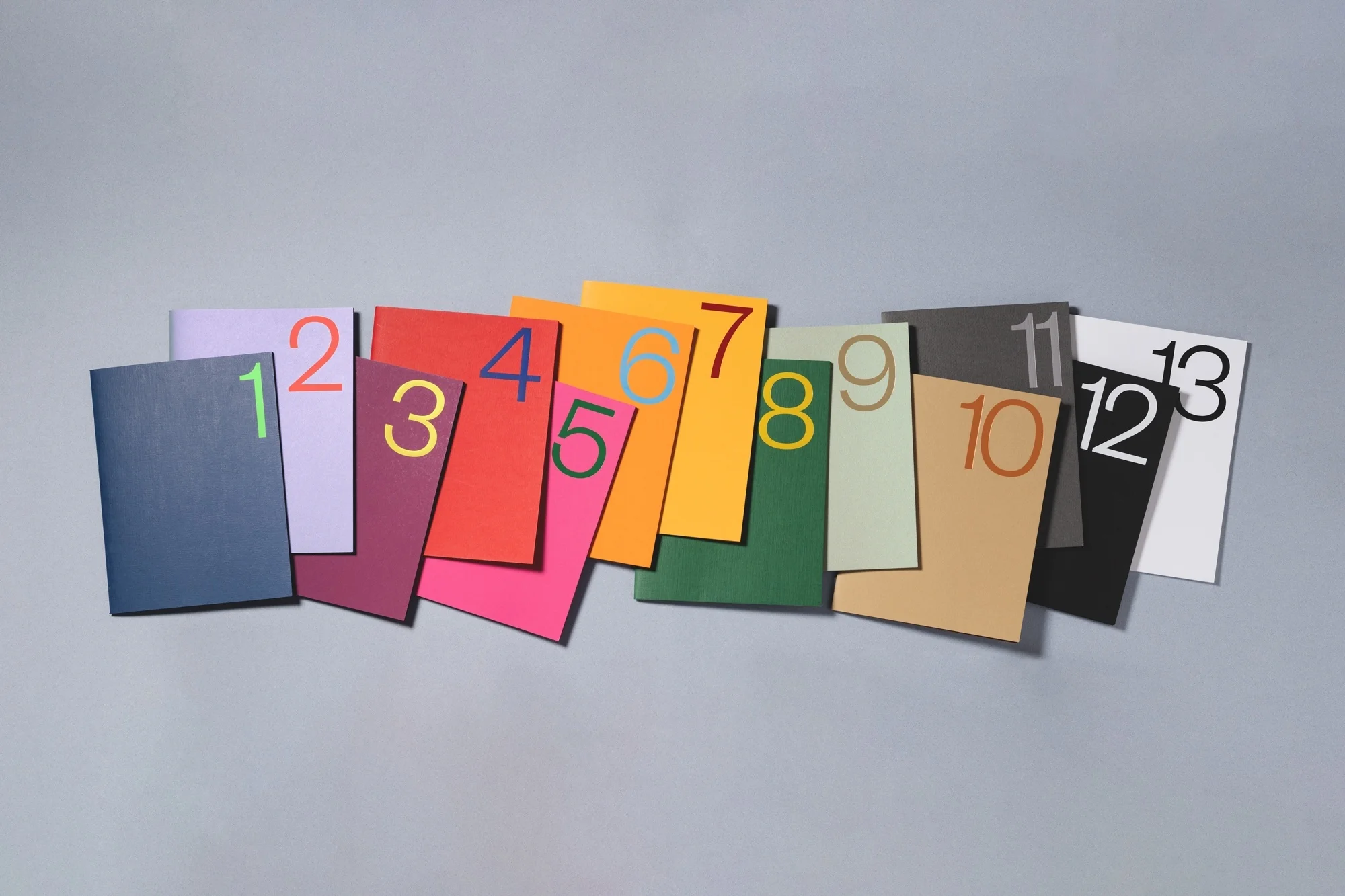 Colorful numbered booklets arranged on a gray surface, including green, purple, red, pink, orange, yellow, and earth-toned colors.