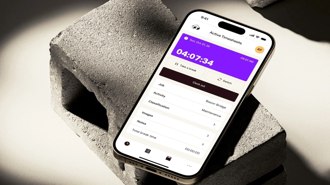 Smartphone displays time-tracking app on concrete block, showing time 04:07:34, date Sun, Oct 01, 25, and options for 'Take a break' and 'Clock out'.