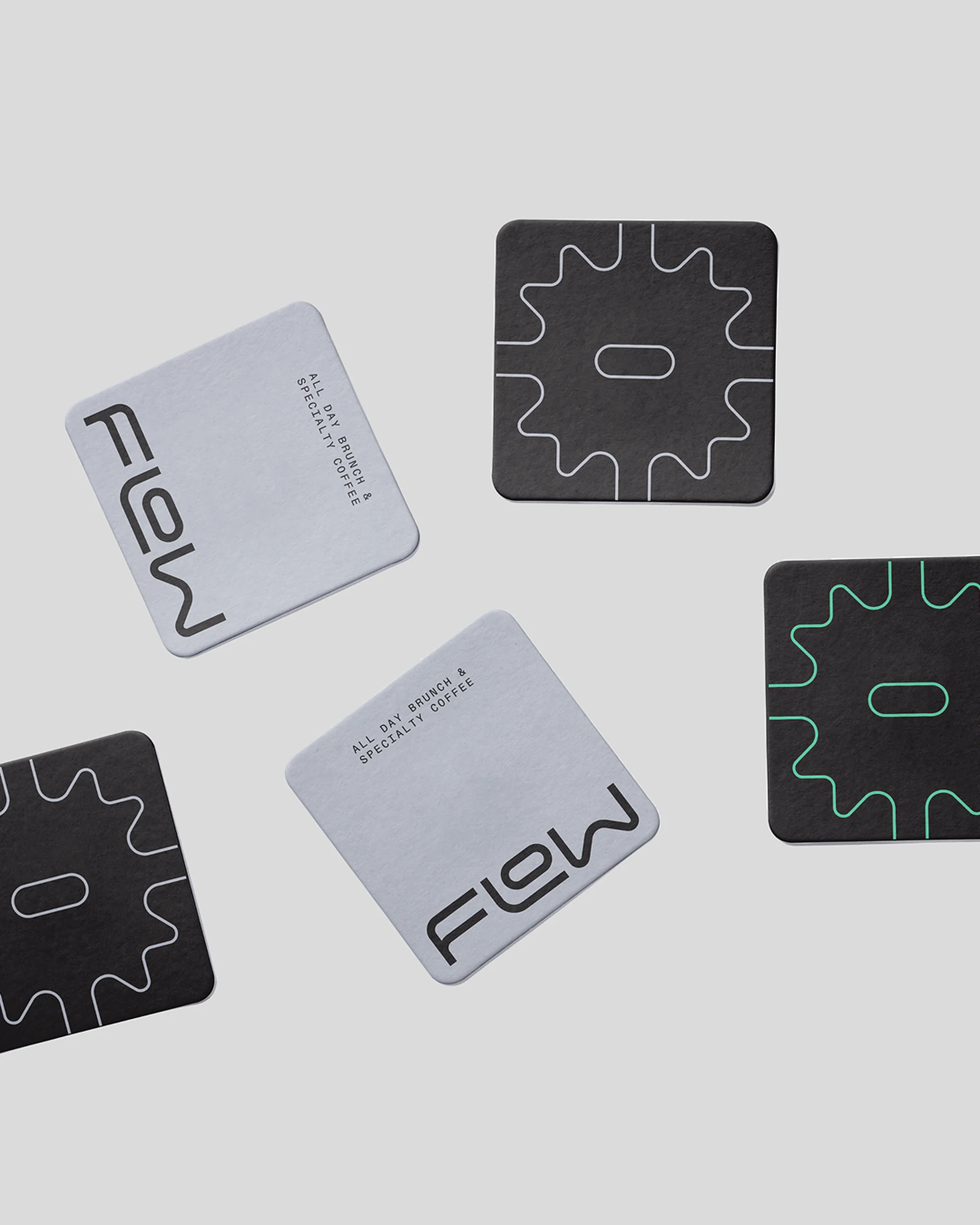 Arrangement of square coasters featuring the 'Flow' logo and cogwheel design on a light gray background. Minimalist branding and design.