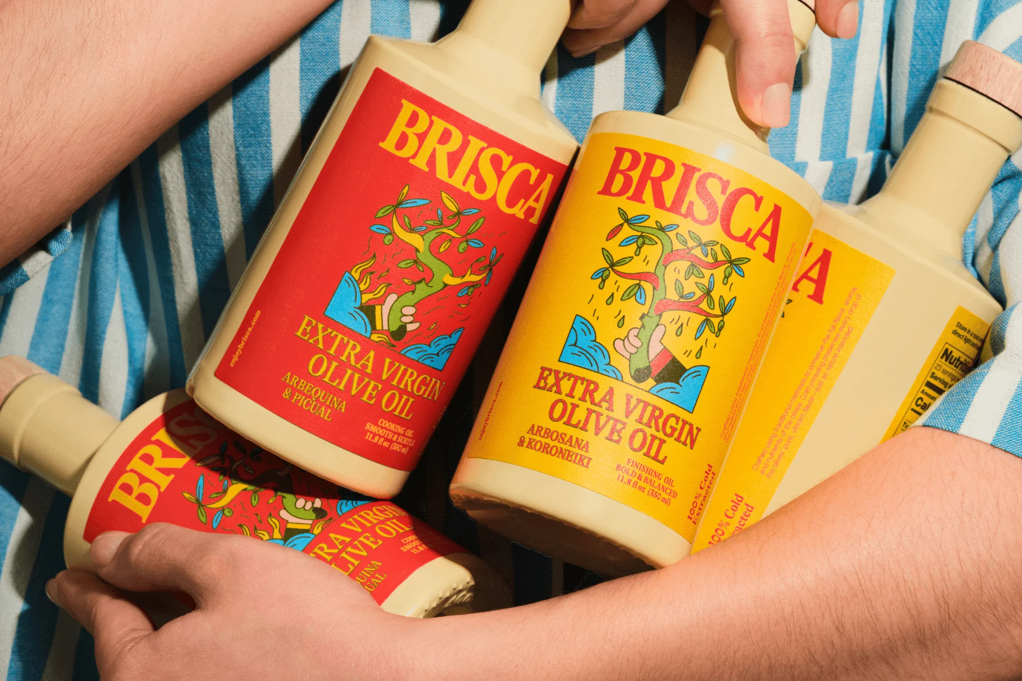 Bottles of Brisco extra virgin olive oil with graphic labels in arms. A collection of olive oil product packaging in hand.