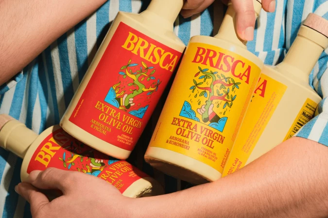 Close-up of a person holding multiple ceramic bottles of Brisca extra virgin olive oil with vibrant red and yellow labels against a blue and white striped shirt background.