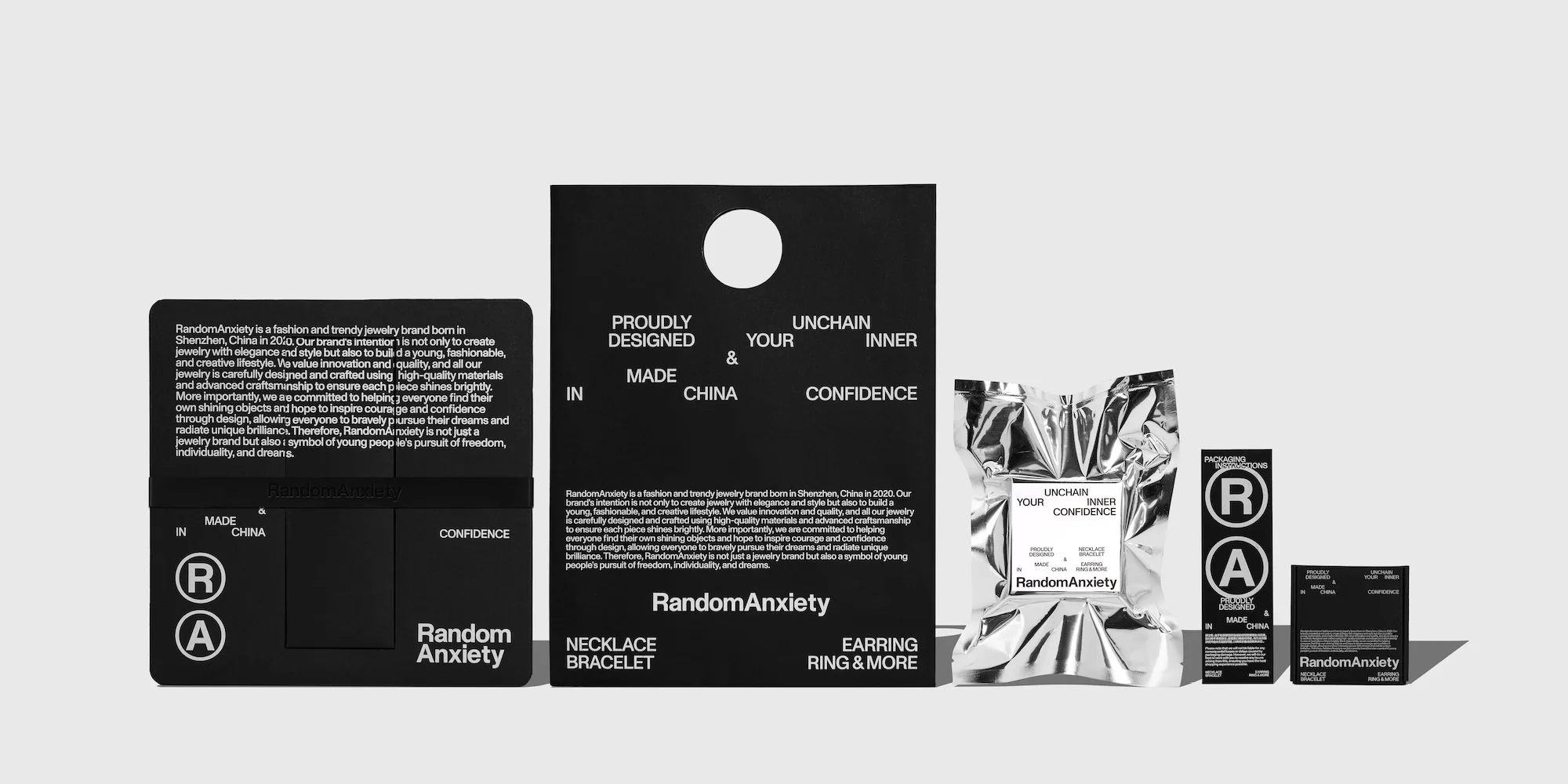Product shot featuring jewelry packaging with Random Anxiety branding, displaying necklace, bracelet, earrings, rings, and more in a studio setting.