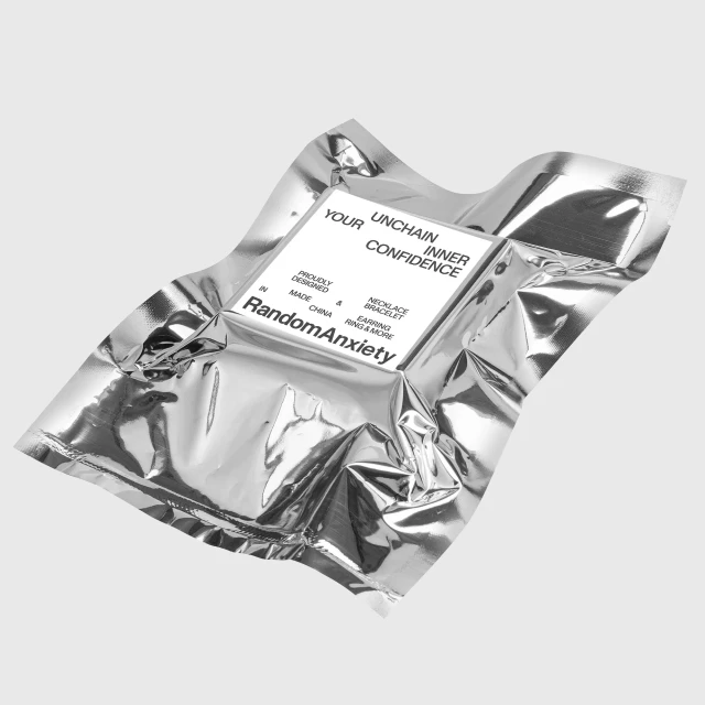 A shiny silver packet, possibly containing jewelry, features a white label with the brand name 'RandomAnxiety' and motivational text.