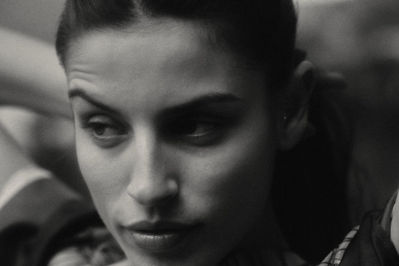Close-up black and white portrait of a woman looking to the left, featuring soft lighting and a shallow depth of field in an indoor environment.