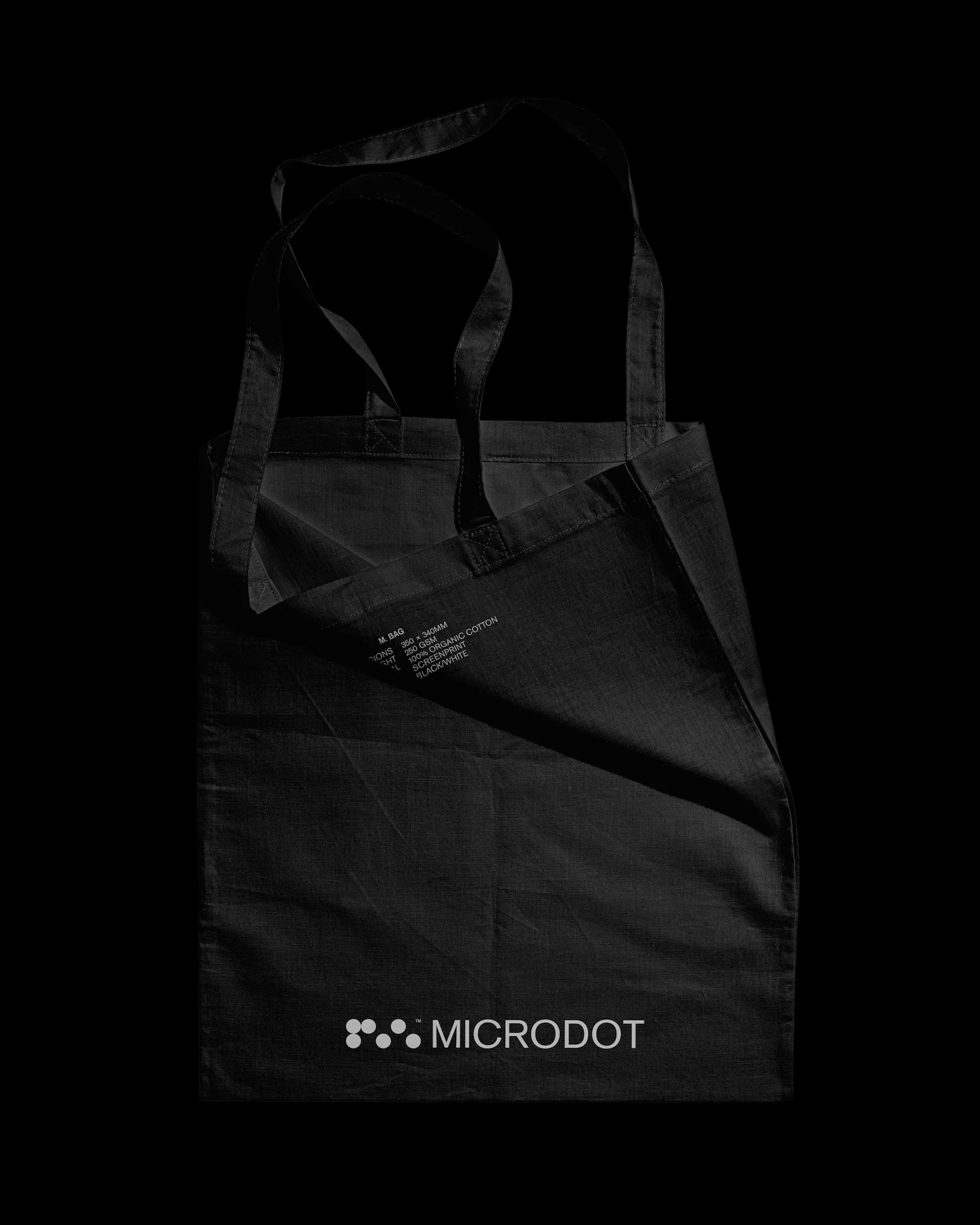Dark cloth tote bag with handles, featuring the 'microdot' logo printed in the corner on a black backdrop.