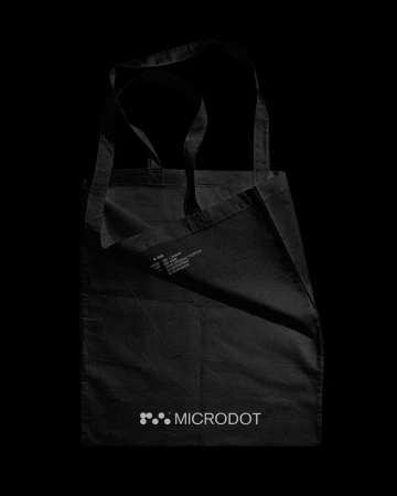 Dark cloth tote bag with handles, featuring the 'microdot' logo printed in the corner on a black backdrop.
