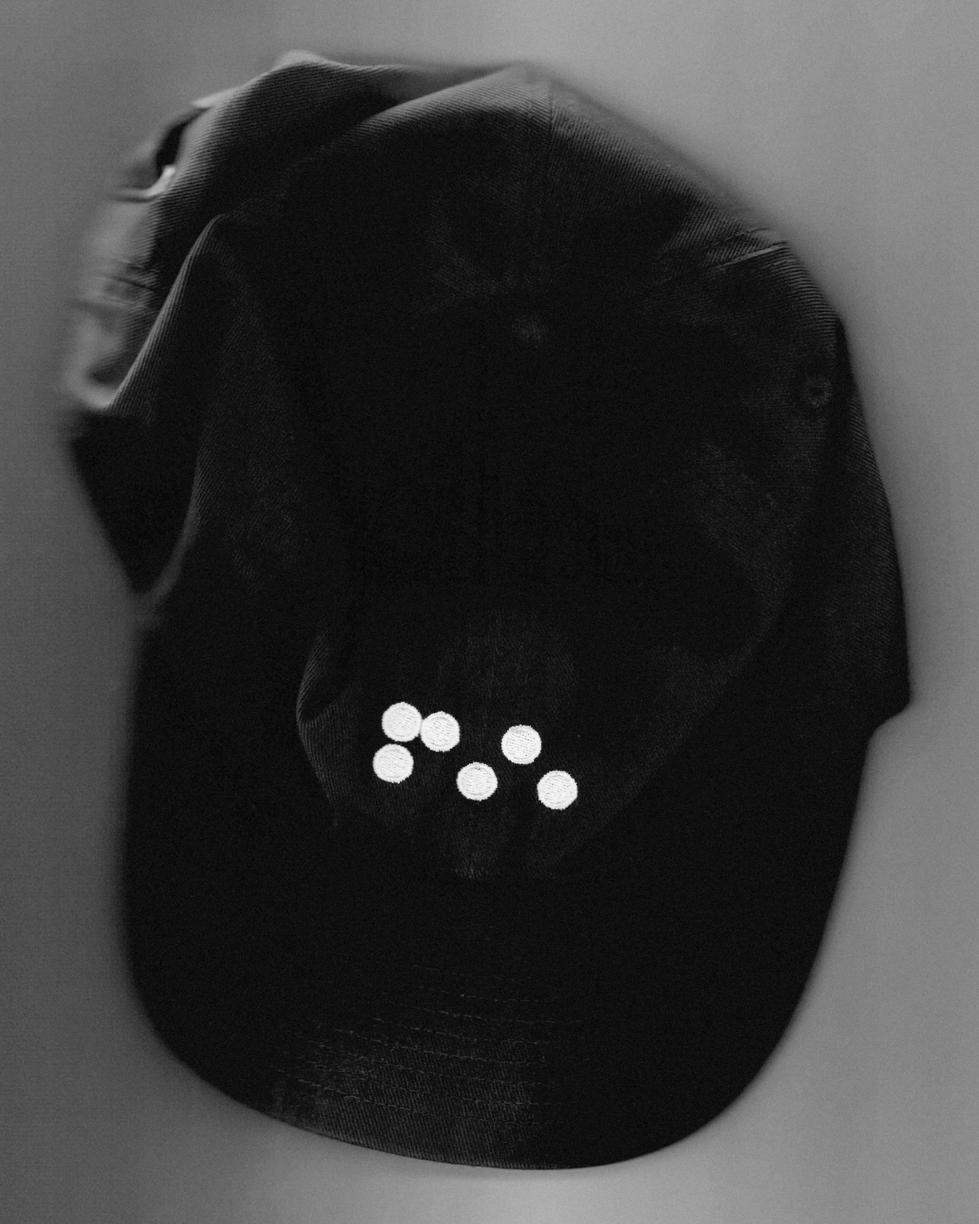 Black and white photo of a dark cap adorned with a cluster of white dots, set against a softly blurred background, creating visual interest.