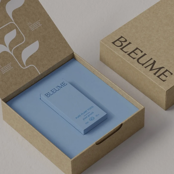 Open brown craft paper box with white botanical illustrations and a blue plant food product resting on a matching blue insert inside.