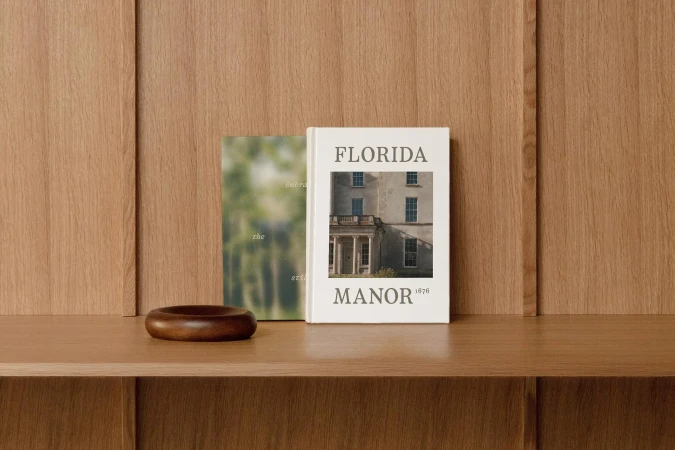 Two hardcover books are displayed on a wooden surface against a wooden paneled wall, creating a warm and inviting atmosphere.