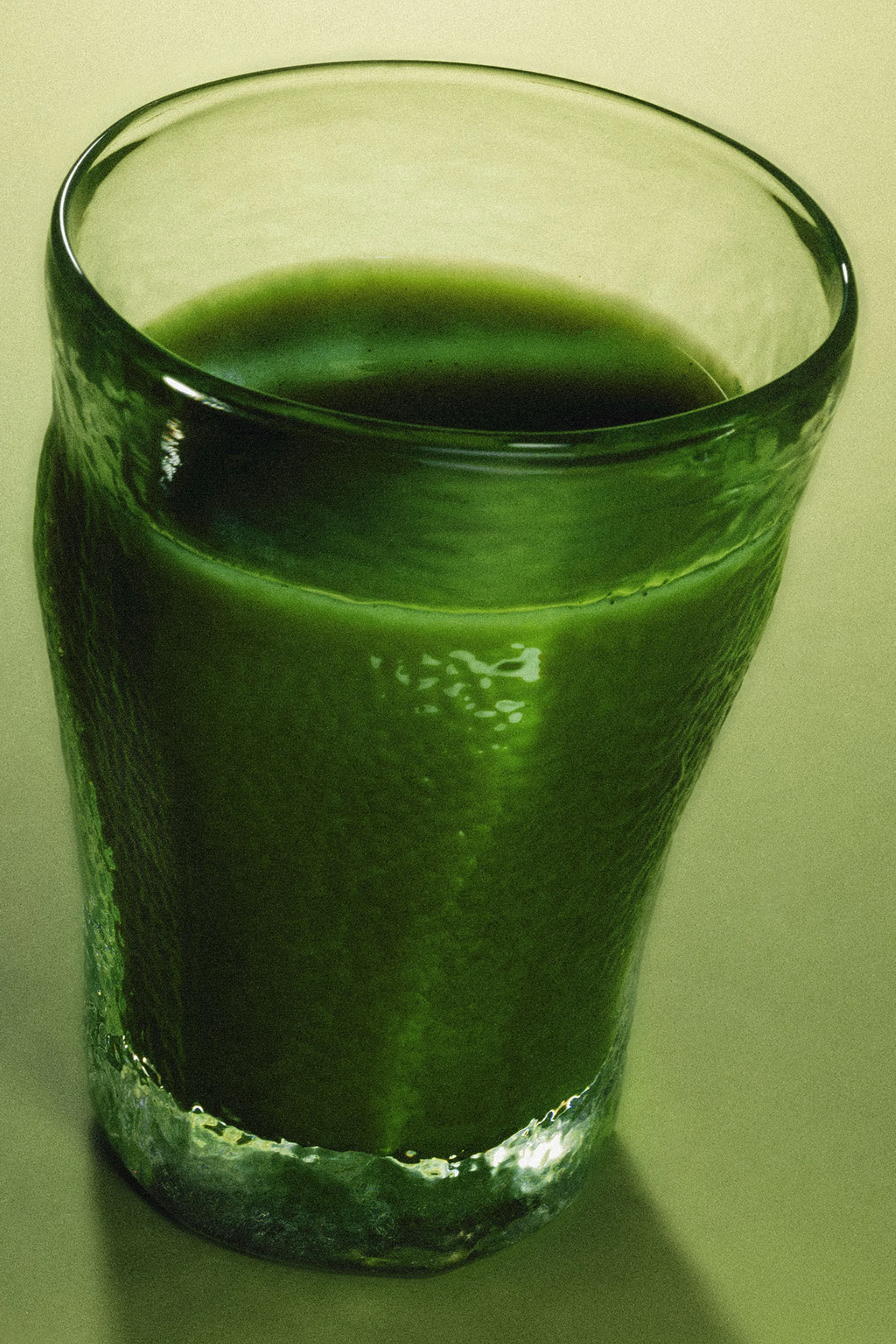 Close-up of a clear glass filled with a vibrant green smoothie, highlighting the drink's texture and color.