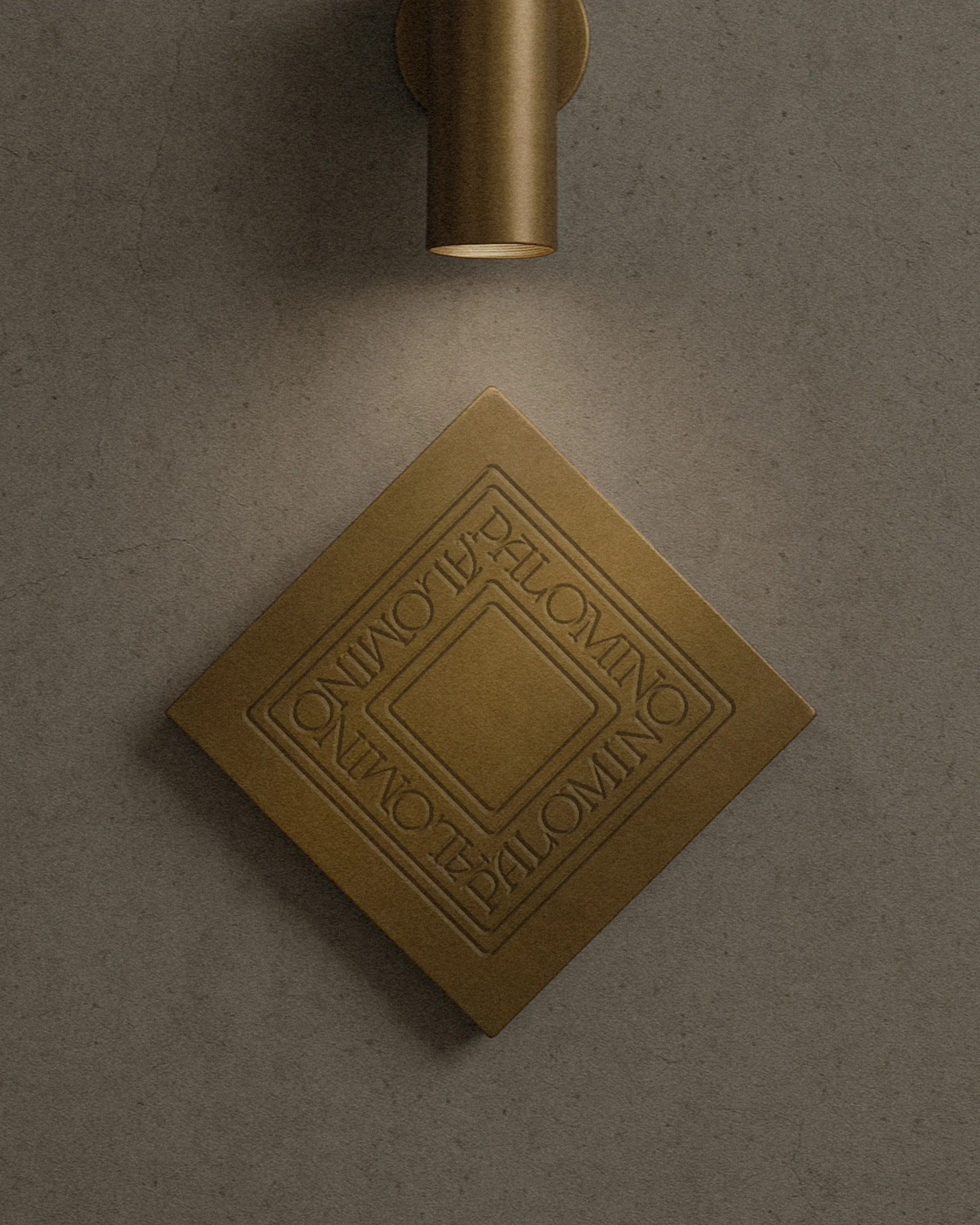 Close-up of a bronze wall sconce illuminating an engraved square tile on a textured gray wall, creating a warm, inviting ambiance.