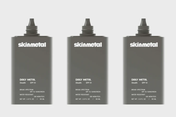 Three identical dark grey Skinmetal Daily Metal SPF 51 sunscreen bottles presented against a plain light grey studio background.