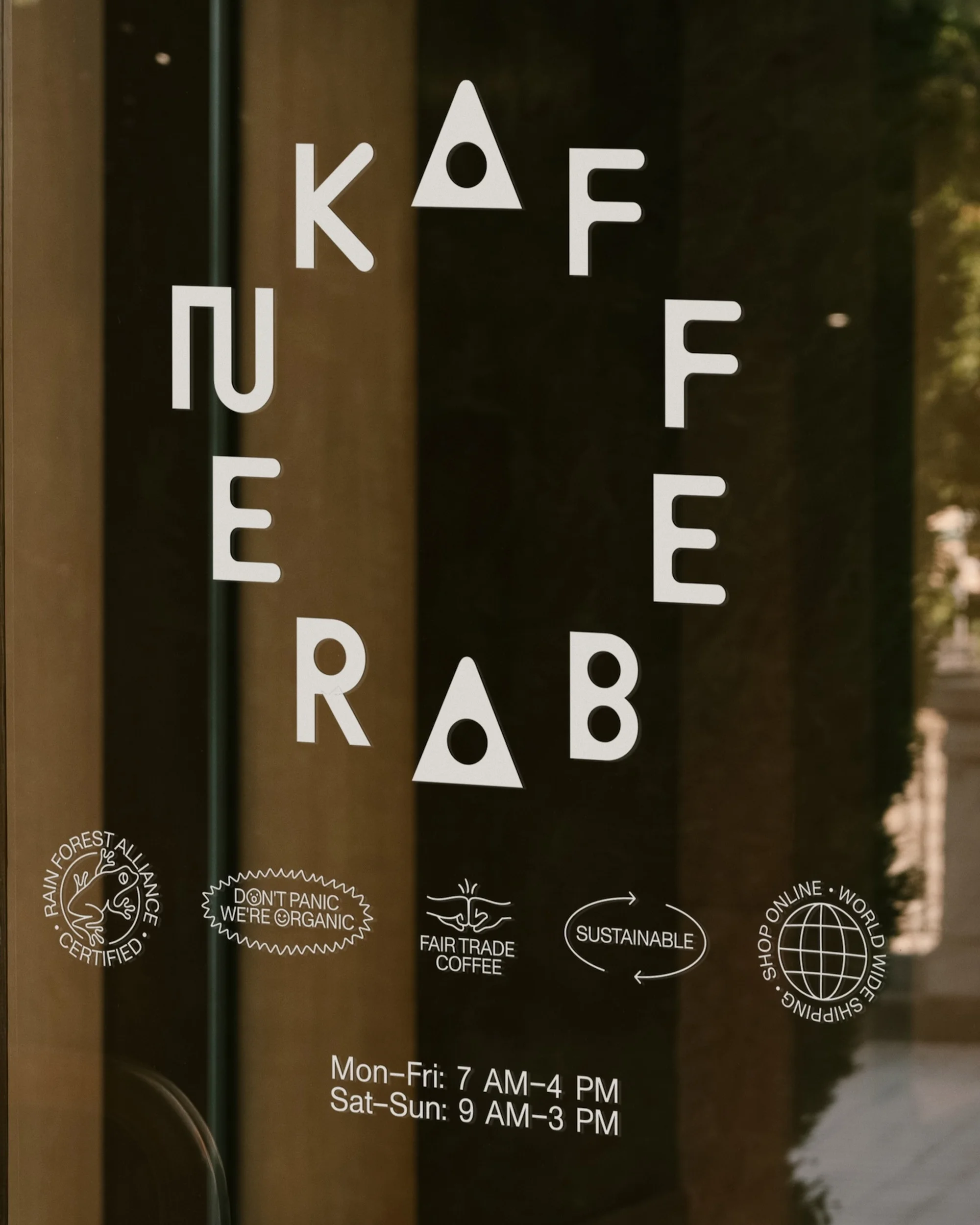 Kaffe Rab text on a glass door with logo marks indicating organic and sustainable practices, displaying shop opening hours.