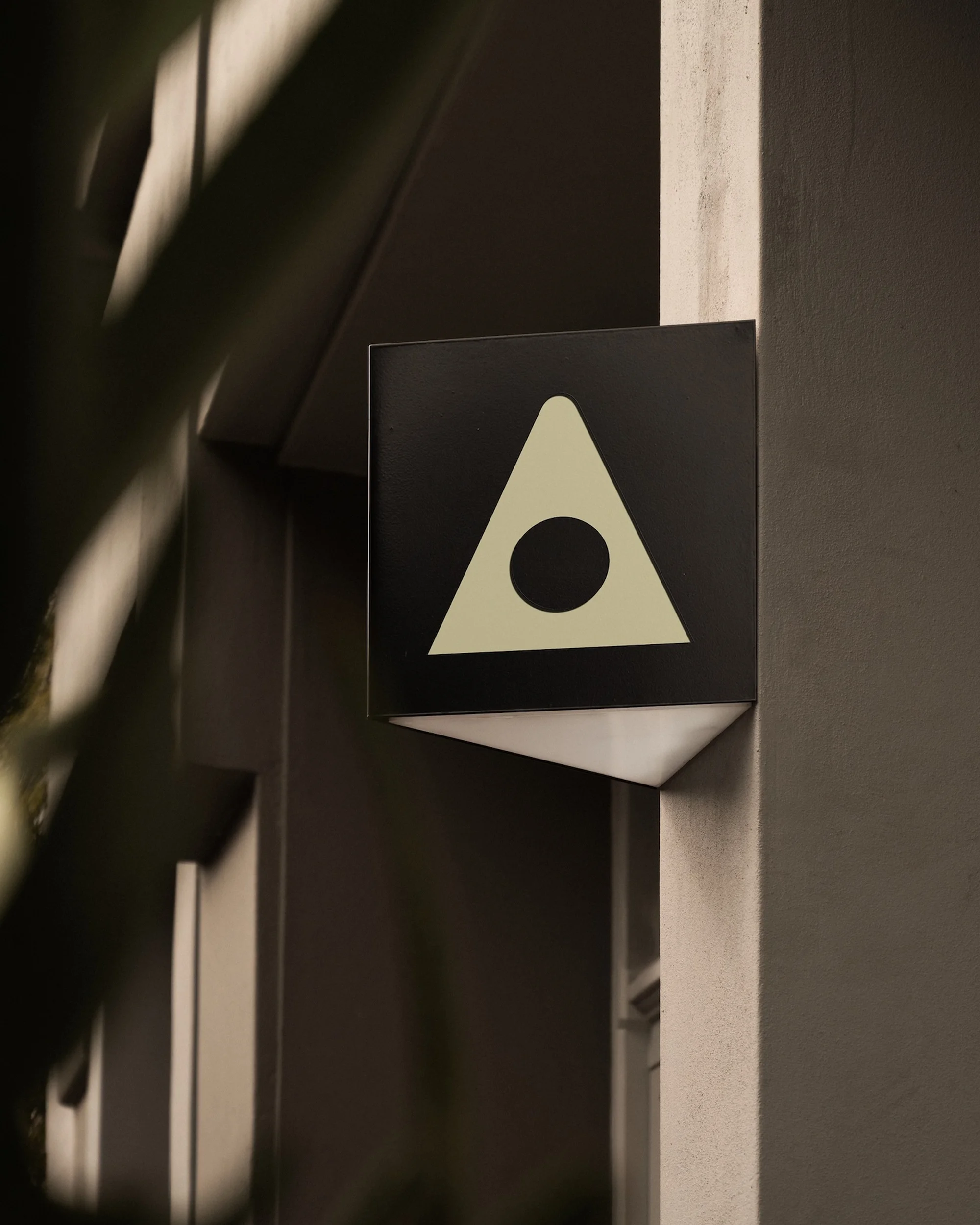 Close-up of a dark sign on a wall with a minimalist graphic design of a triangle shape with a circle in the center.