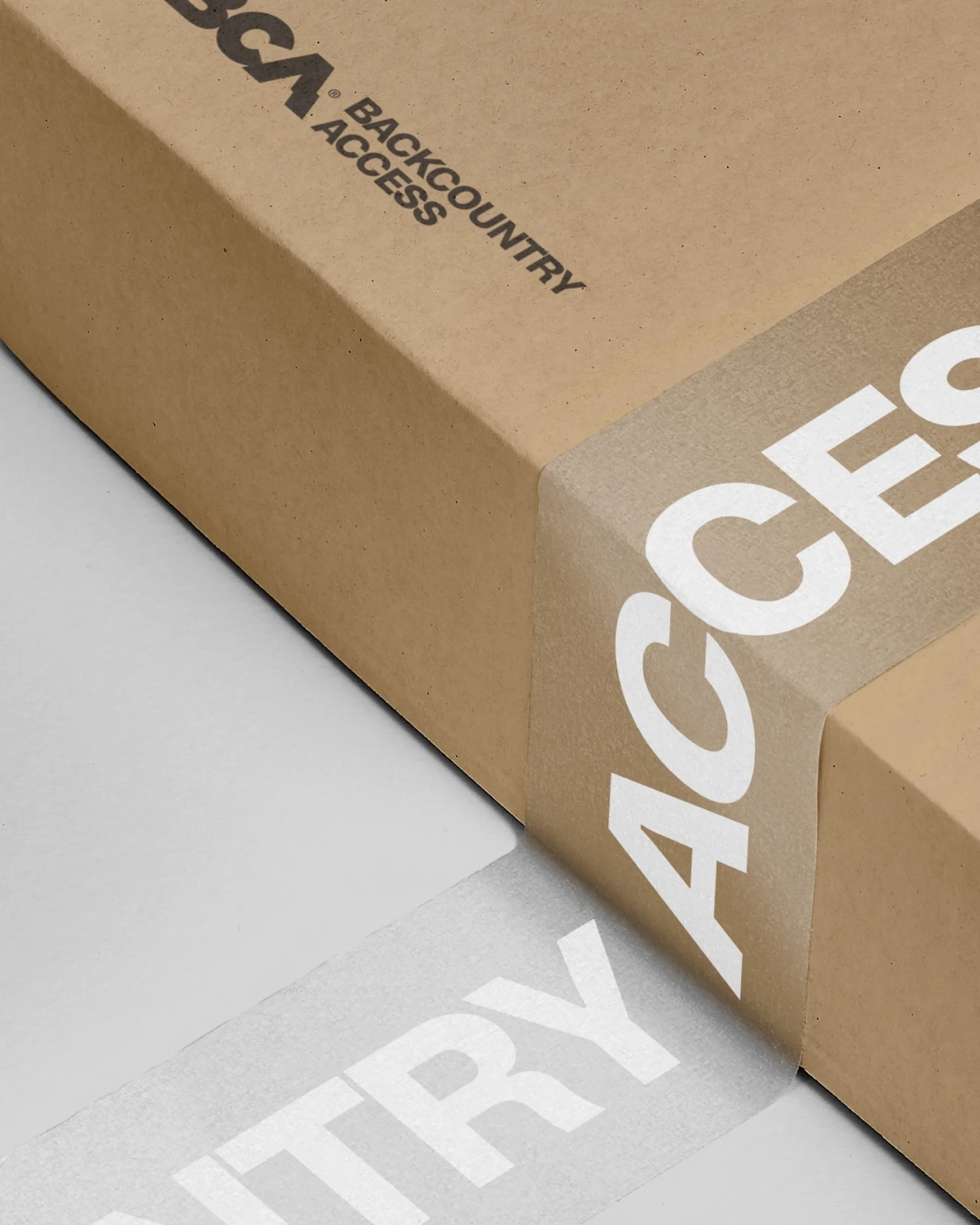 Close-up of a brown cardboard box sealed with branded tape featuring white lettering spelling out 'ACCESS' repeatedly, set against a grey background.
