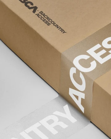 Close-up of a brown cardboard box sealed with branded tape featuring white lettering spelling out 'ACCESS' repeatedly, set against a grey background.