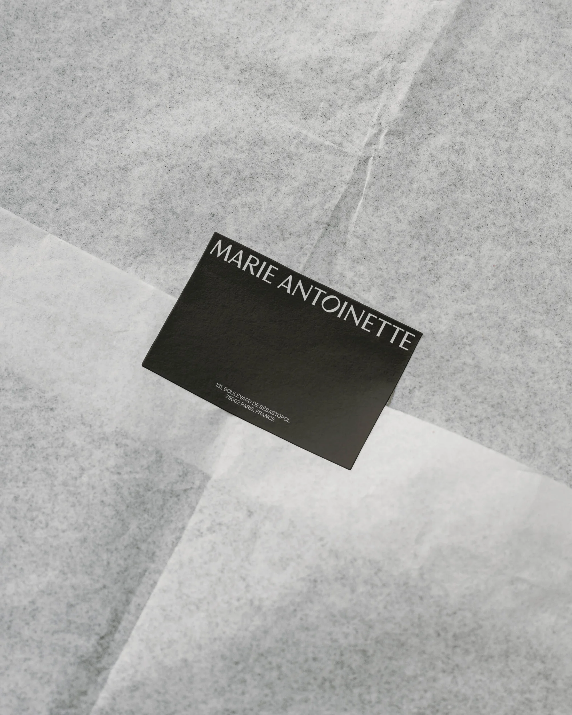 Promotional card with the brand name MARIE ANTOINETTE on white tissue paper. Elegant and simple design for fashion and beauty.