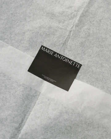 Promotional card with the brand name MARIE ANTOINETTE on white tissue paper. Elegant and simple design for fashion and beauty.
