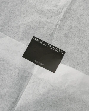 Black rectangular business card featuring the Marie Antoinette brand name centered on crumpled white tissue paper.