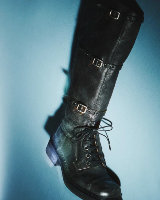 Tall black leather boot with buckles and laces on a light blue background, fashion footwear for editorial use.