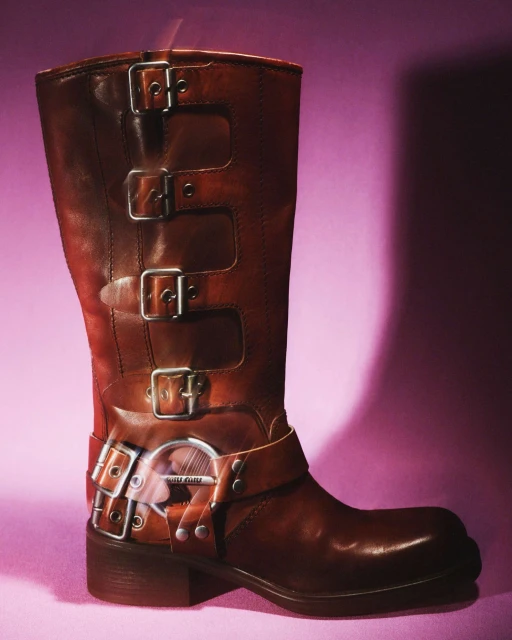 Studio shot of a brown leather mid-calf boot with multiple buckles and straps against a gradient pink and purple background.