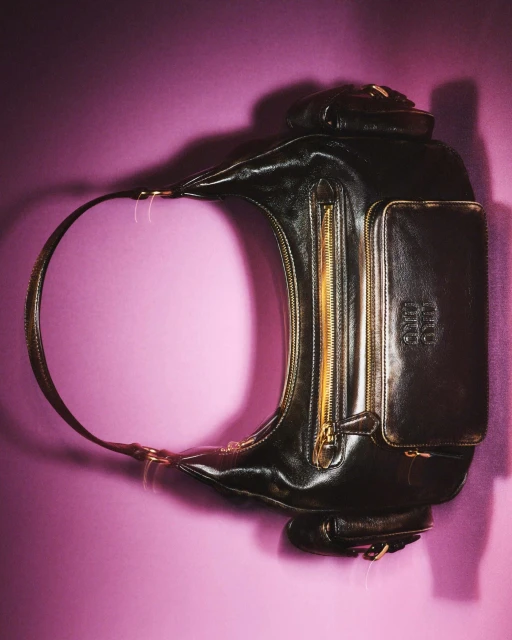 Elegant black leather handbag with a gold zipper and a handle, set against a vibrant purple backdrop, showcasing fashion accessory.