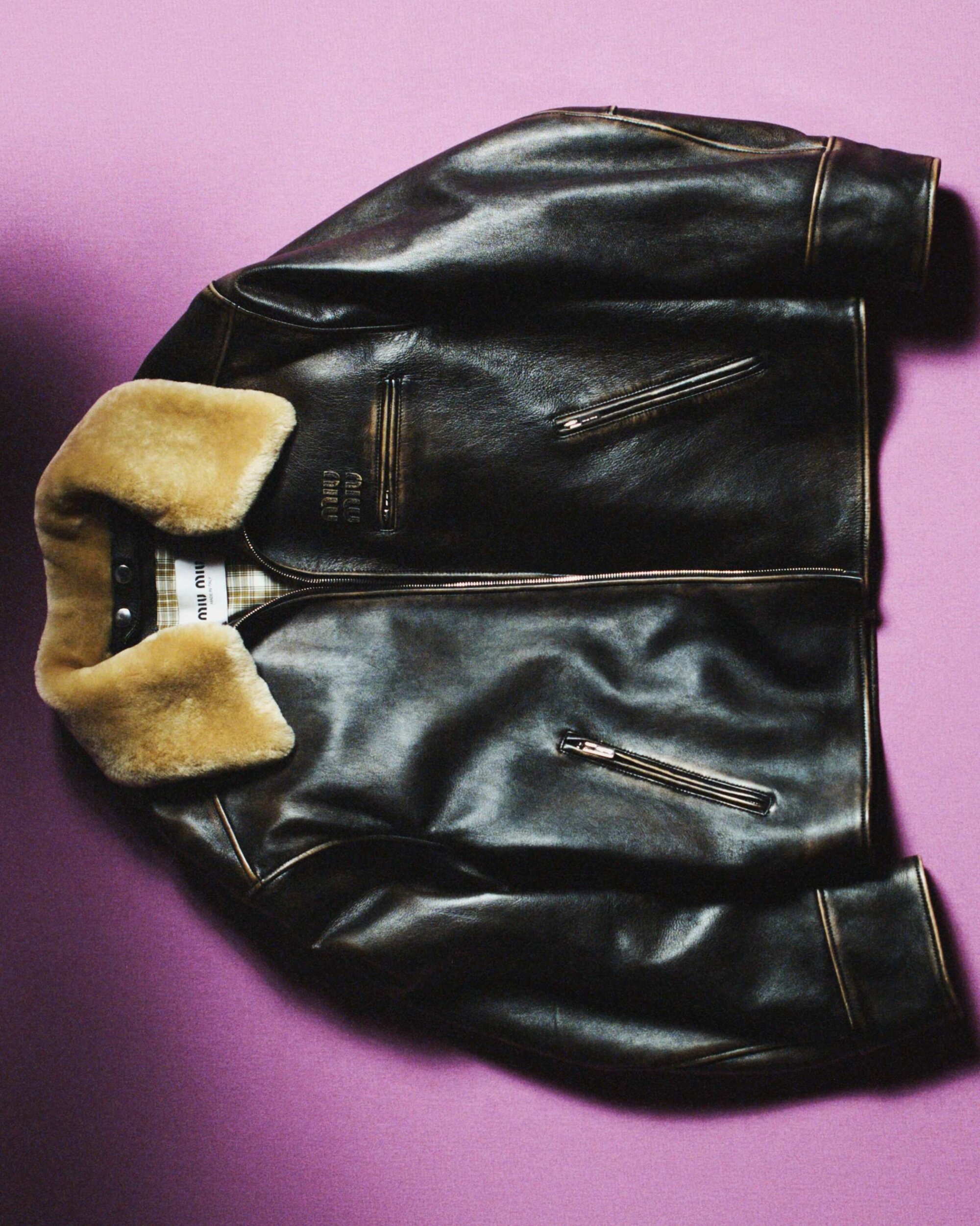 Studio shot of a brown leather jacket with a shearling collar on a purple background, showcasing fashion apparel and garment details.
