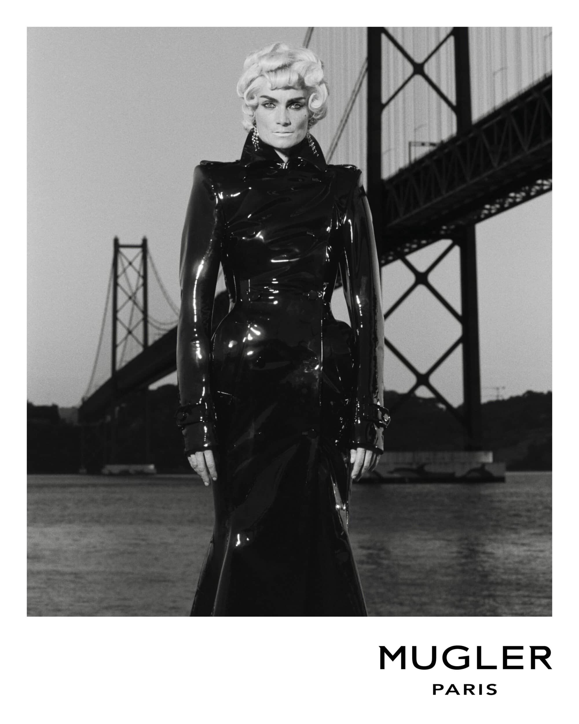 Fashion shot of a woman in a black latex dress with a bridge in the background, grayscale image.