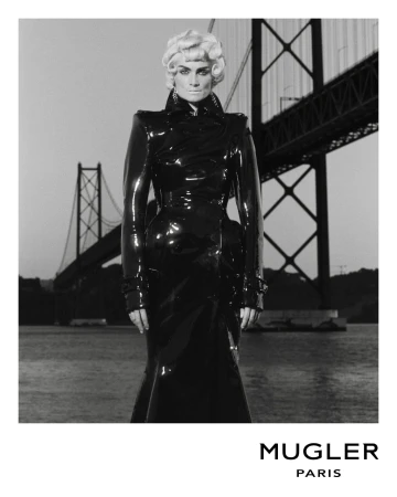 Fashion shot of a woman in a black latex dress with a bridge in the background, grayscale image.