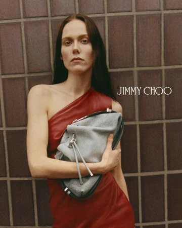 Model Kiki Willems in a red dress holding a grey handbag against a tiled wall for Jimmy Choo Spring 2026