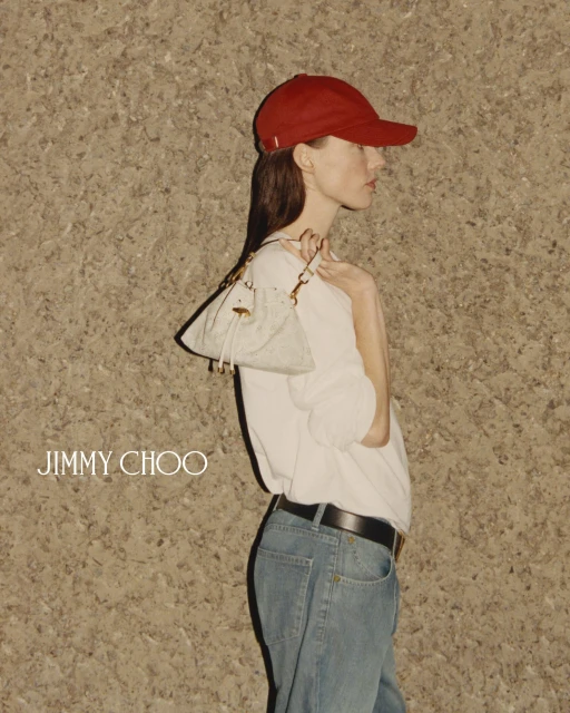 Fashion shot of a woman wearing a red baseball cap, light blue jeans, and a white top, holding a small purse in an indoor setting.
