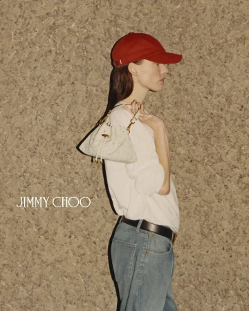 Fashion shot of a woman wearing a red baseball cap, light blue jeans, and a white top, holding a small purse in an indoor setting.