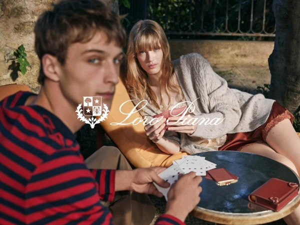 Two attractive adults relax outdoors playing cards at a round table in a sun-dappled, green garden with dappled light.