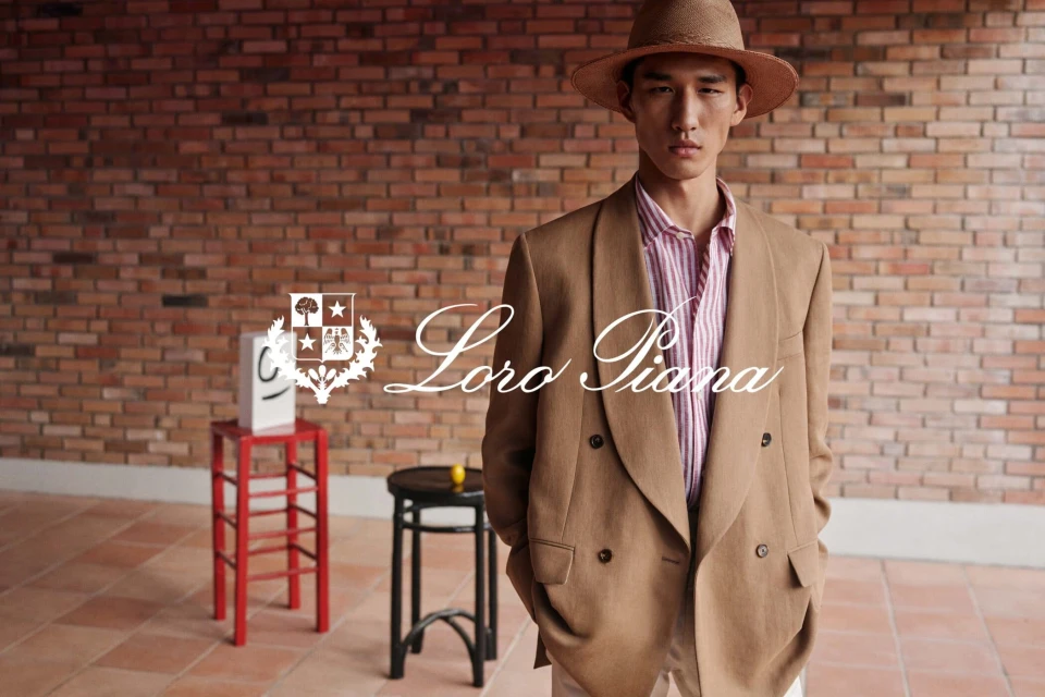 Asian male model wears a straw hat and brown double-breasted blazer in a fashion editorial with a brick wall backdrop and logo.