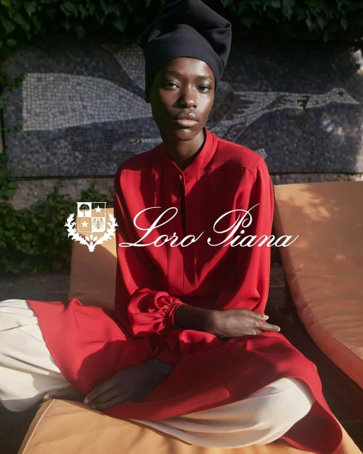 An adult woman is seated in red long-sleeve shirt and light pants, wearing a black head covering, with 'Loro Piana' text overlay.