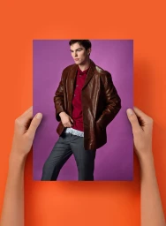 Two hands holding a printed photograph of Nicholas Hoult in a brown leather blazer against a purple backdrop