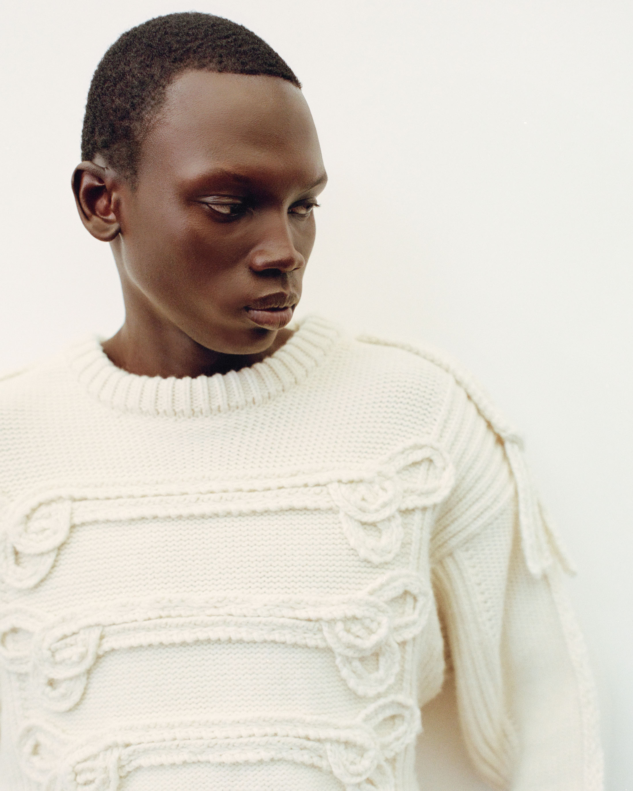 Portrait of an adult Black male wearing a textured cream-colored knit sweater, set against a neutral background in an indoor setting.