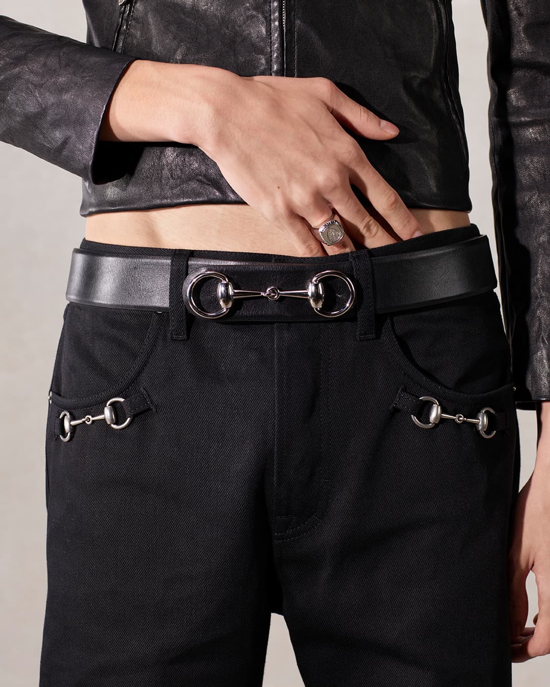 Close-up of a person wearing black denim jeans and a black leather belt with a horse bit buckle and a black leather jacket.